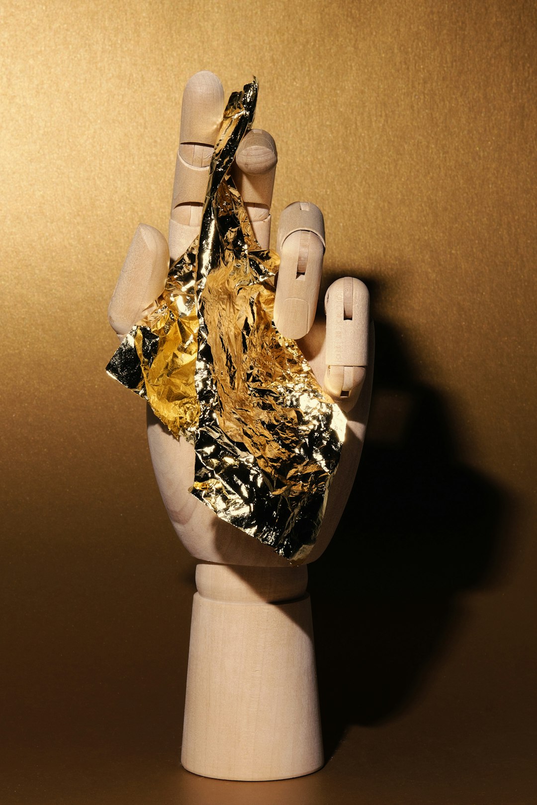 Wooden hand holding crumpled gold foil against gold background.