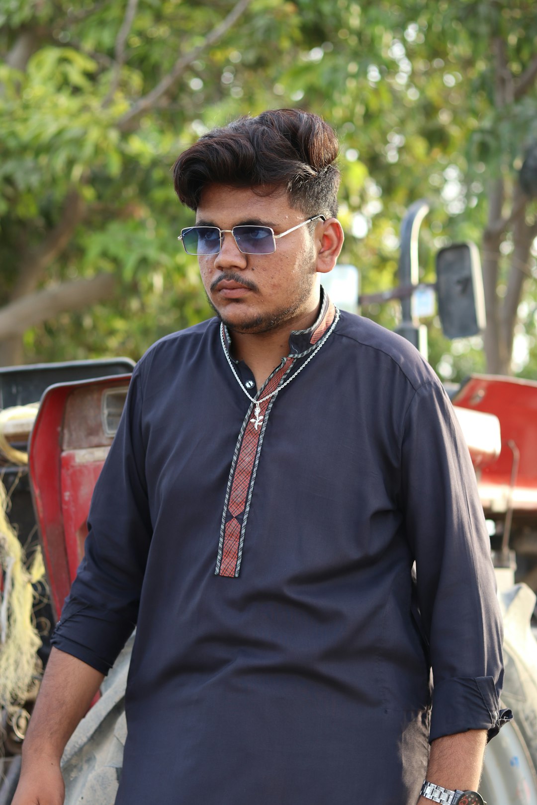 a man in a blue shirt and sunglasses standing in front of a tractor