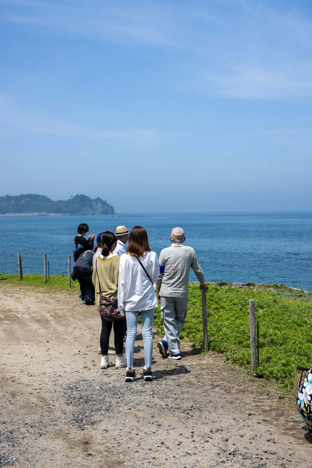 a group of people walking down a dirt road next to the ocean