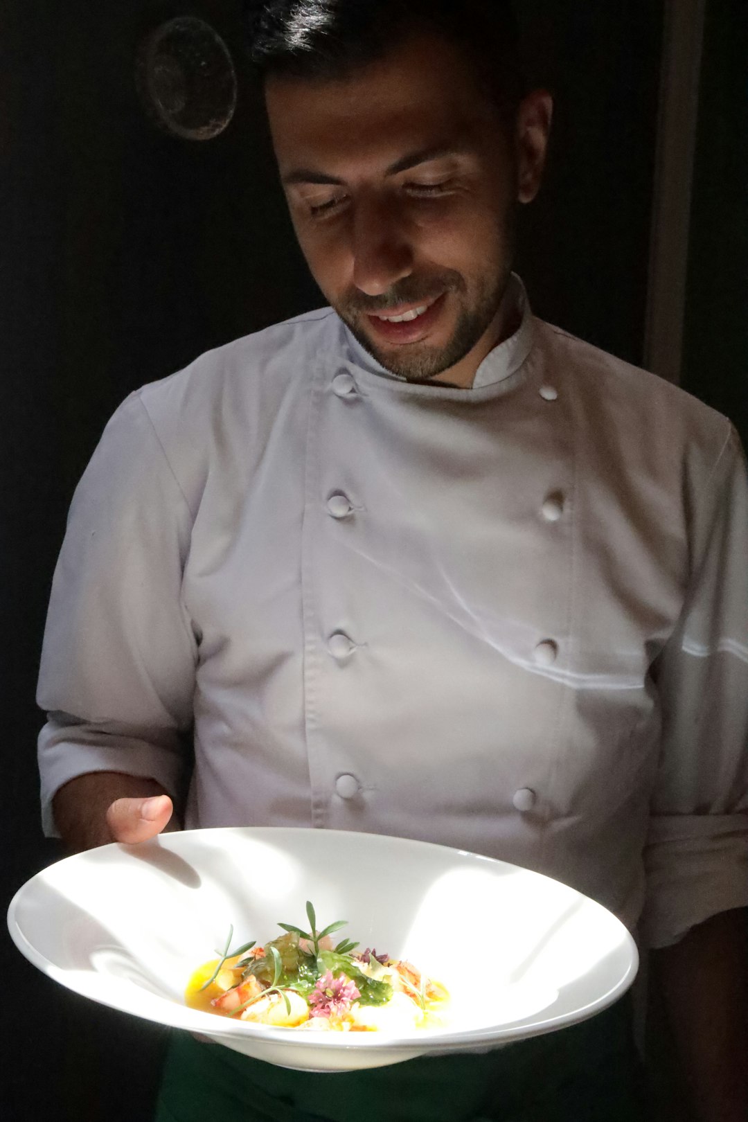 A chef presents a plate of food with a smile.