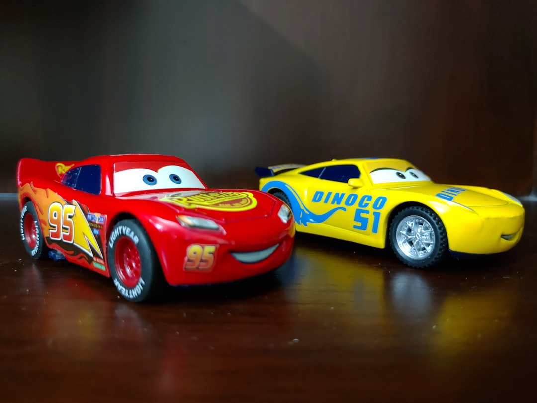 two red and yellow Disney Cars plastic toys on brown wooden surface