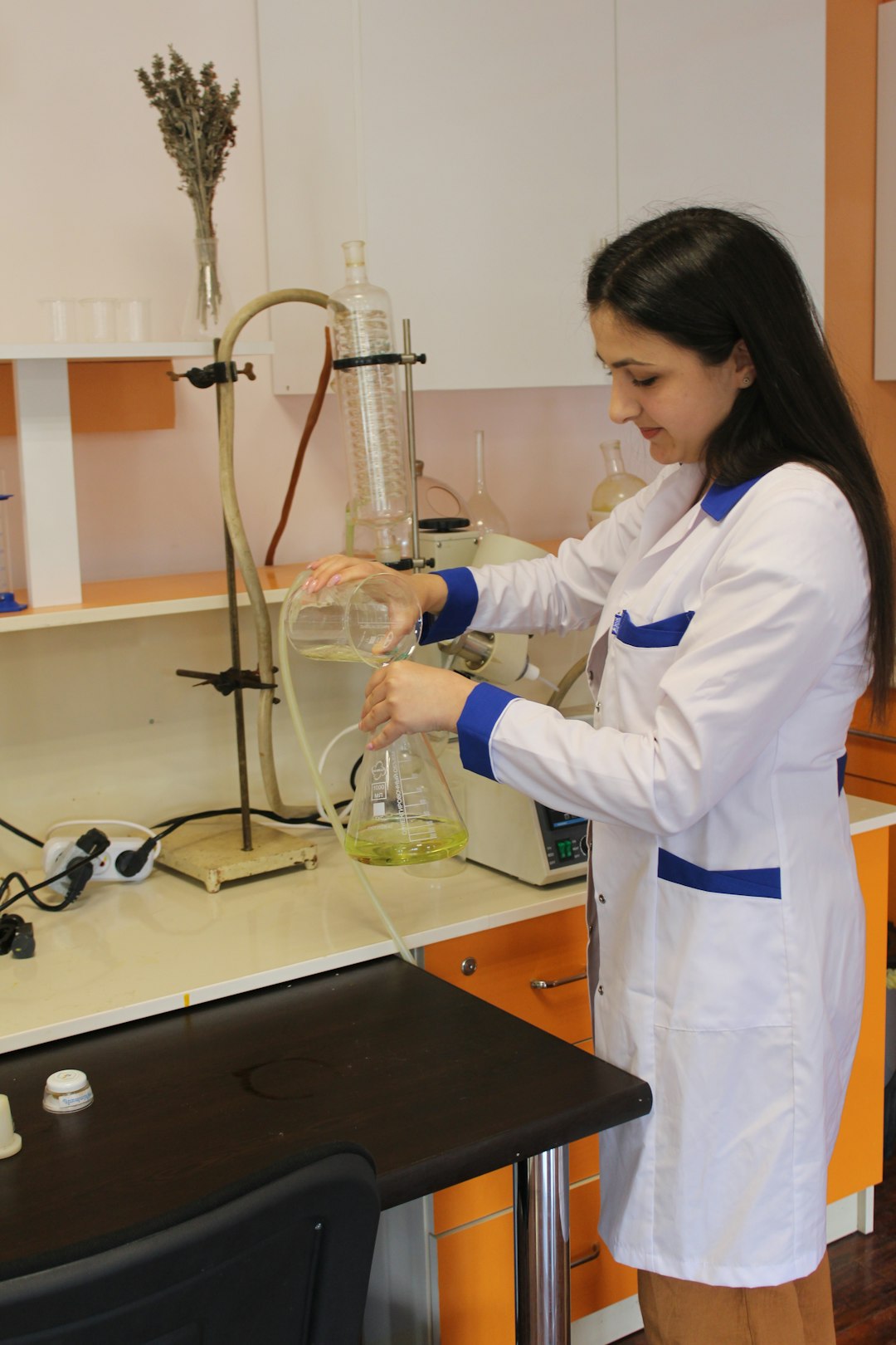 a woman in a lab coat pouring liquid into a beakle