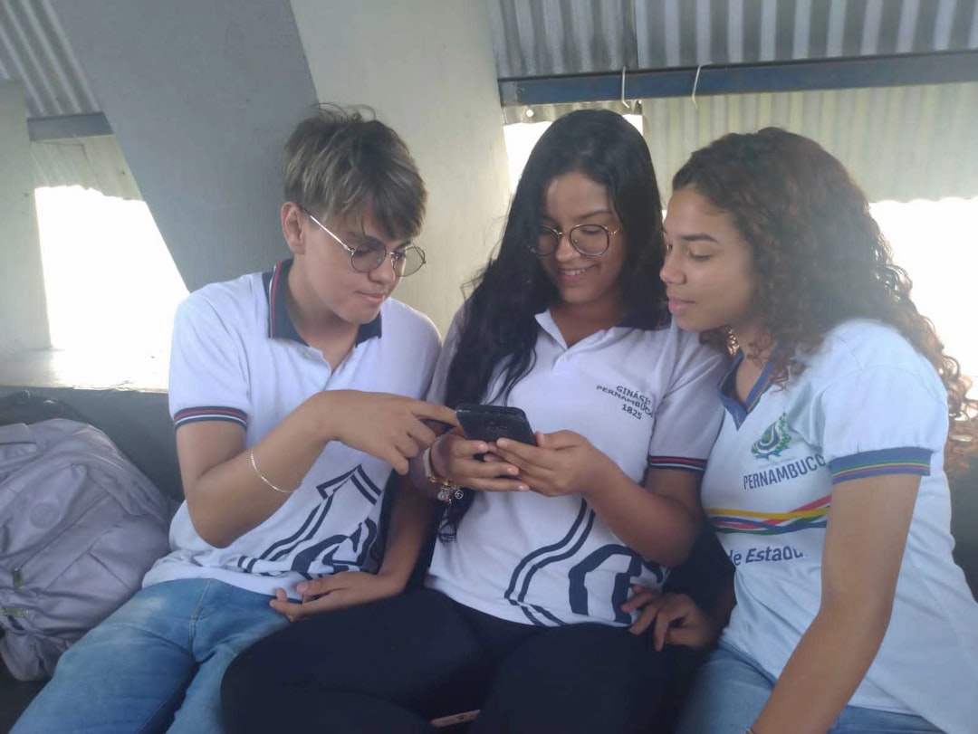three girls sitting on a couch looking at a cell phone