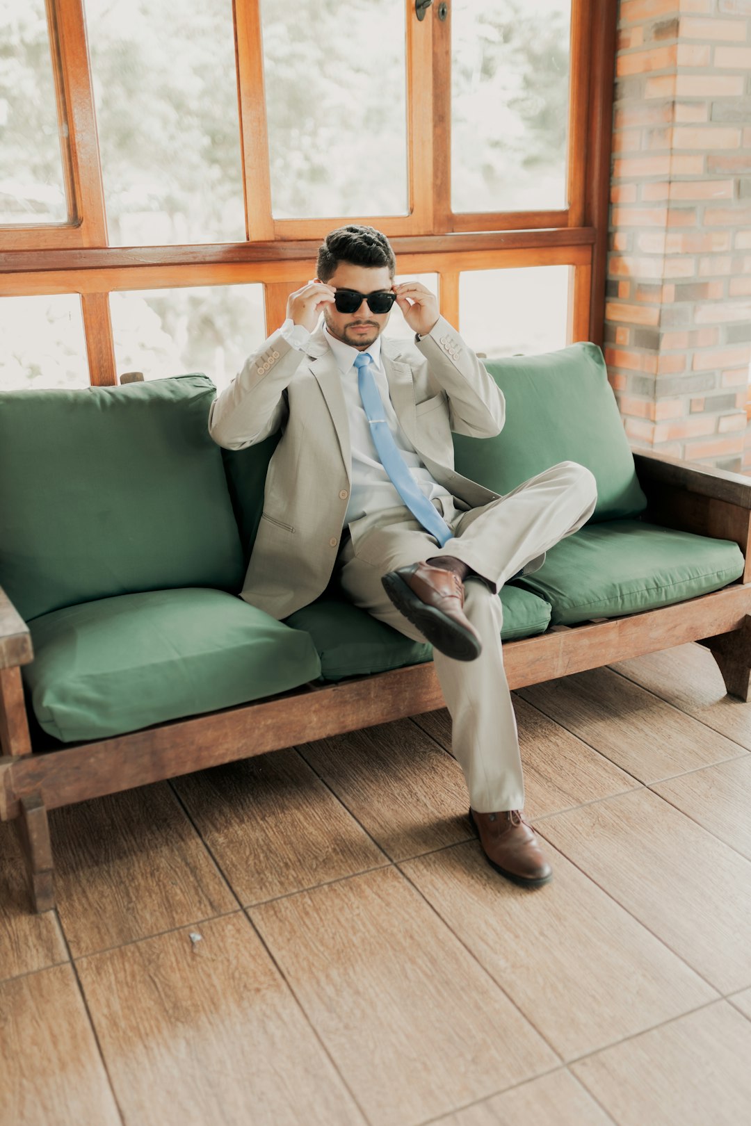 Man in a suit adjusts sunglasses on a green sofa.