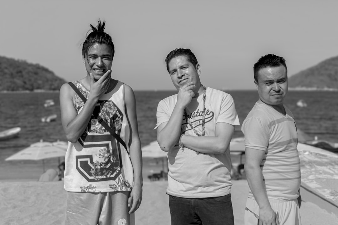 Three people stand on a beach with thoughtful expressions.