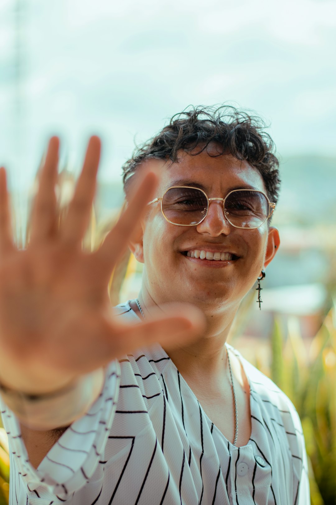 Man in sunglasses holds hand up, smiling