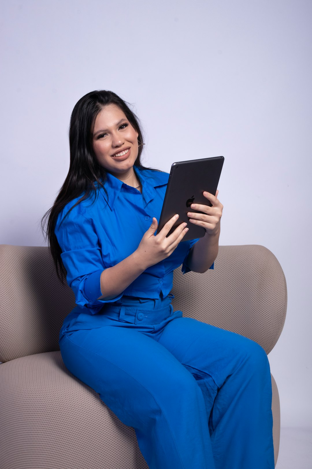 Young woman in blue suit holds tablet while sitting on sofa.