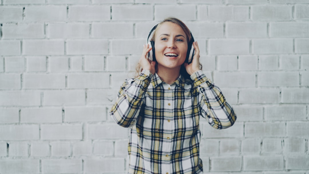 Woman wearing headphones and smiling against brick wall