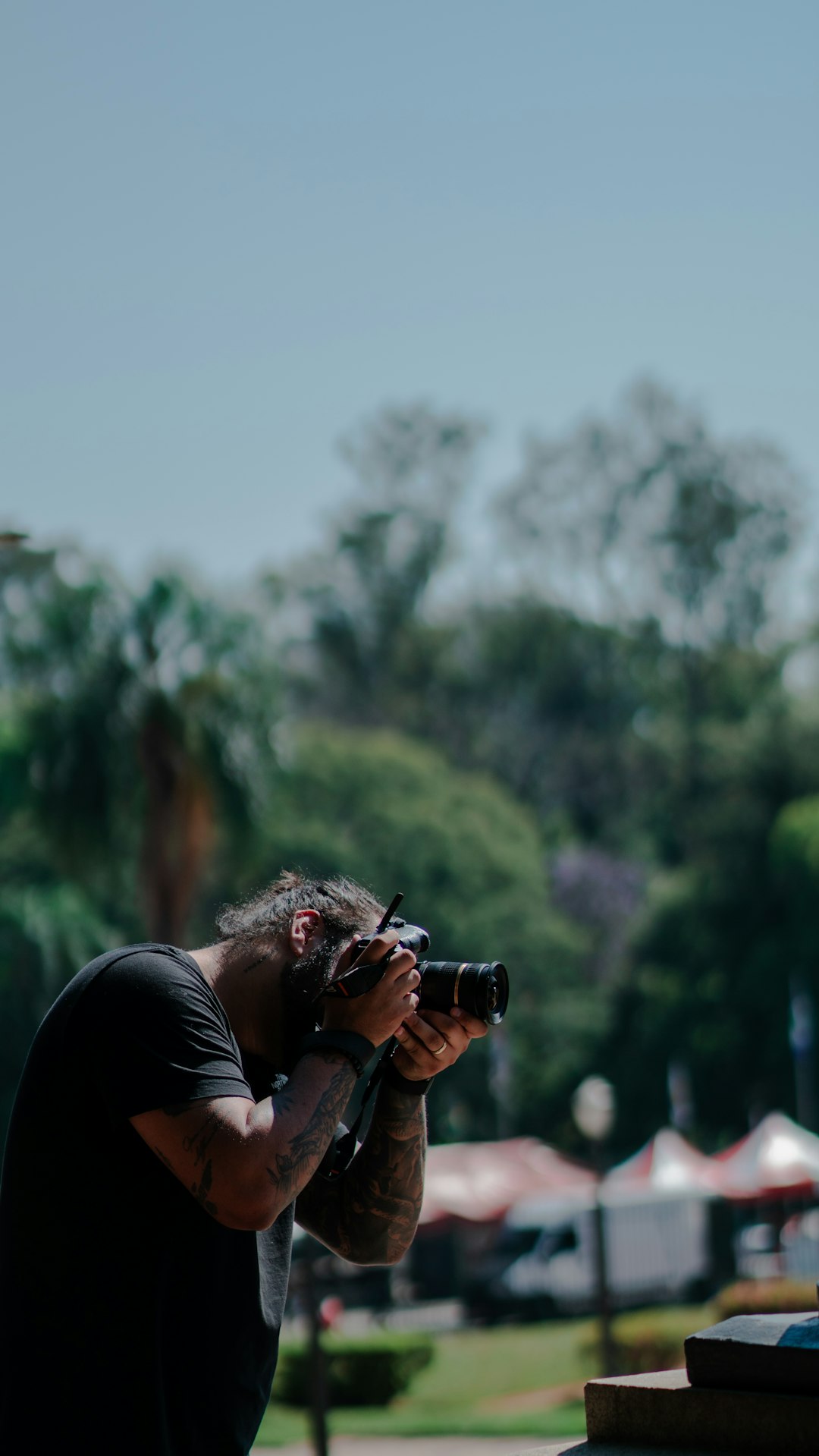 Man with tattoos taking a picture with a camera.