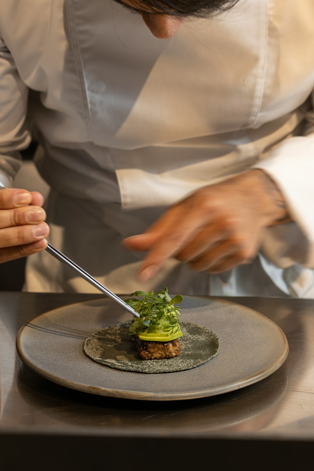 Chef carefully plating a gourmet dish with tweezers.